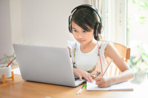 Little,Asian,Girl,Sitting,At,Home,At,A,Table,Using